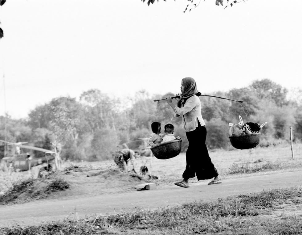 AVietnamesemothercarriesherchildreninoneoftwobasketsattachedtoasticksheholdsoverhershoulderinBenSucVietnamJan171967.jpg